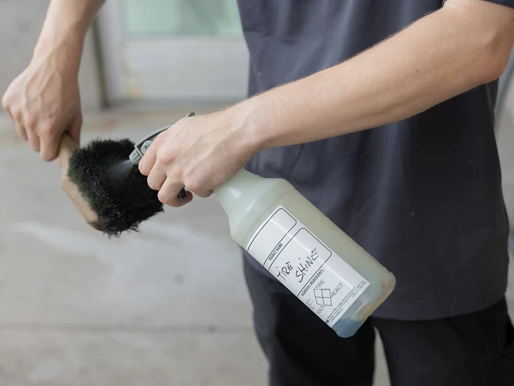 Detailer spraying tire shine onto a brush