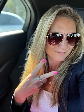 Caitlin A. Donovan in aviator sunglasses and a navy blazer, making a peace sign with signature pink nails.