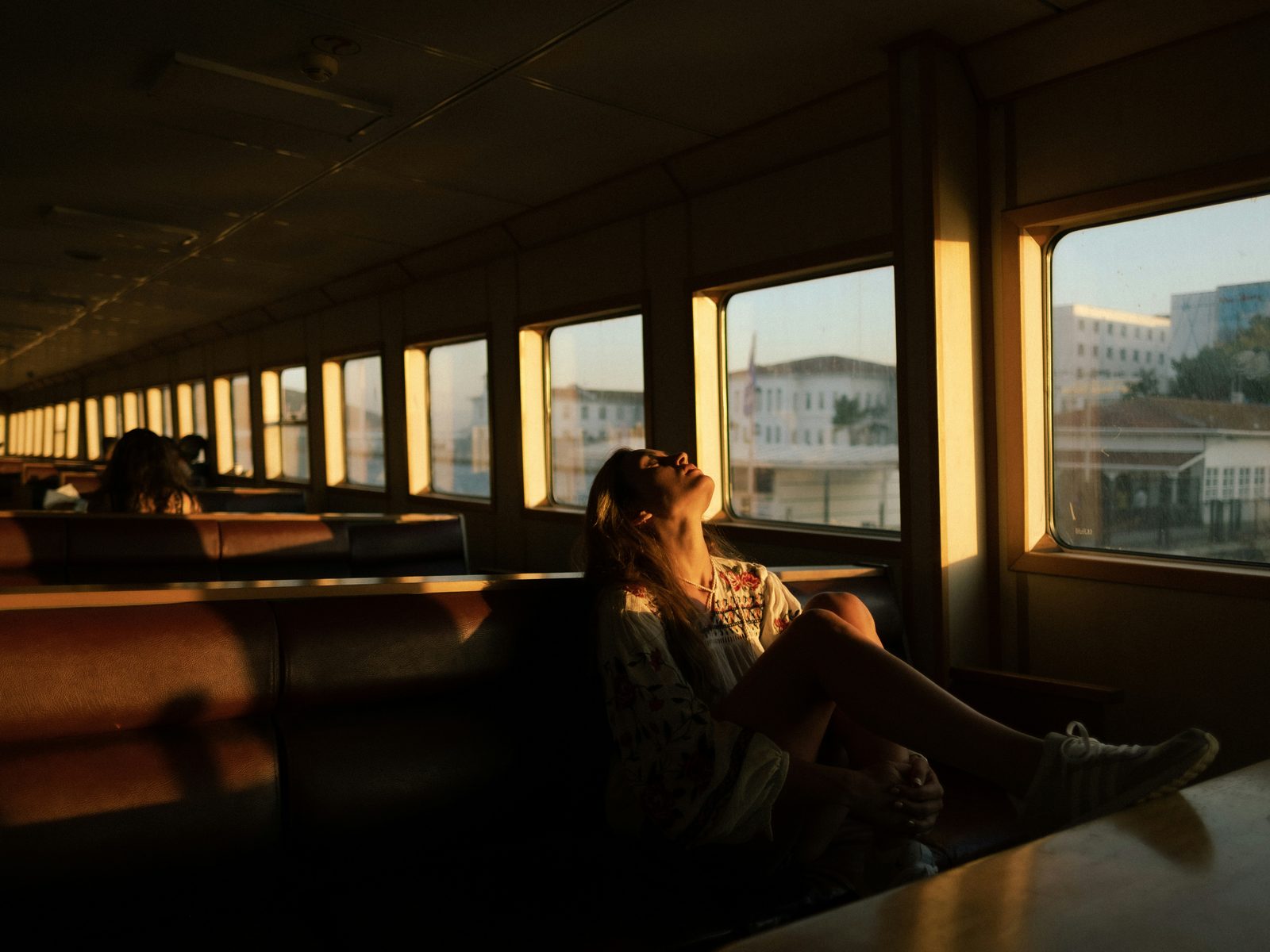 Passenger leaning back beside a sunlit train window.