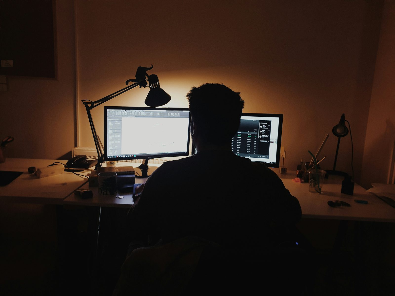 Professional working at a desk with two monitors late at night.