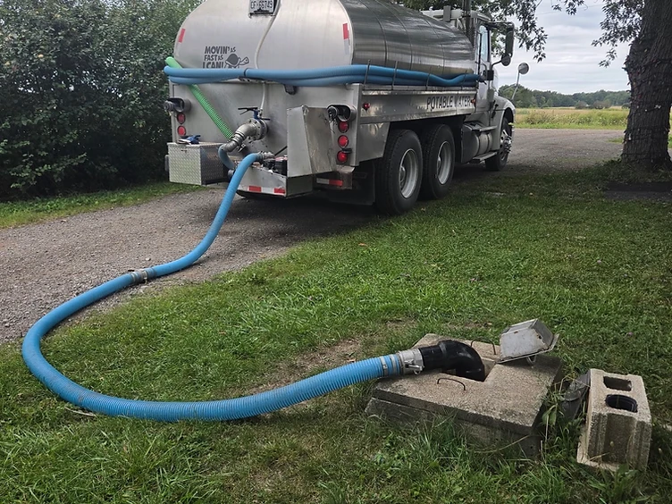 Duncan's Water Delivery truck actively filling an in-ground cistern with a blue hose