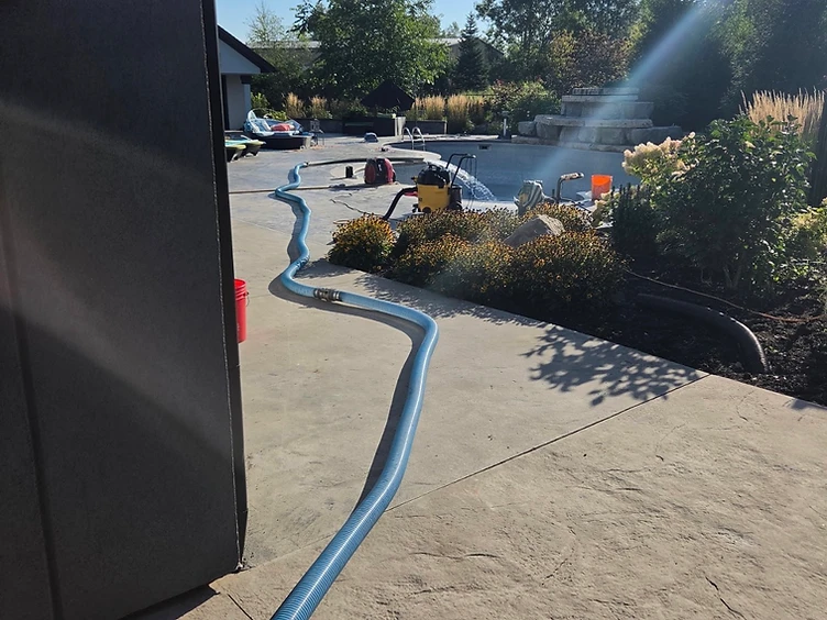 Blue water delivery hose running across the yard toward a pool-filling job