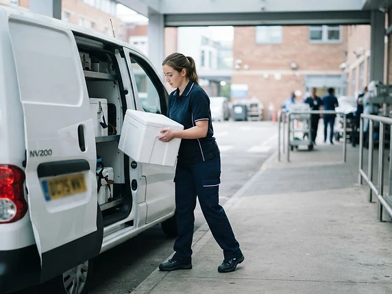 Healthcare courier loading a delivery van outside a hospital