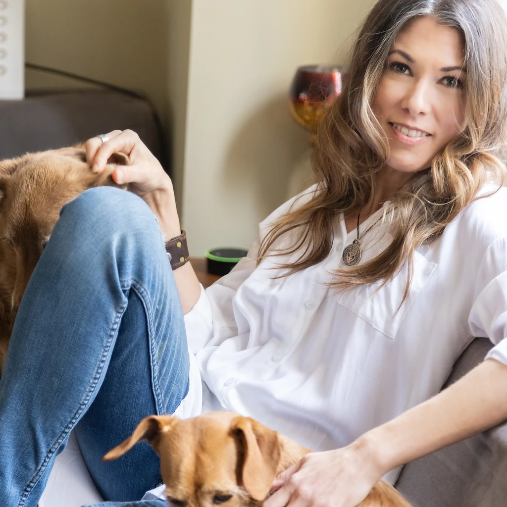 Kimberly Artley seated on a couch with two dogs, illustrating the relationship at the heart of her work