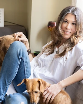 Kimberly Artley seated on a couch with two dogs, illustrating the relationship at the heart of her work