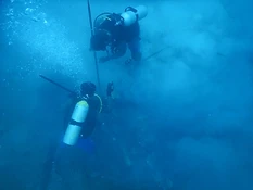 Two divers surveying the submerged wreck debris field at Ontong Java Atoll, one releasing a stream of bubbles