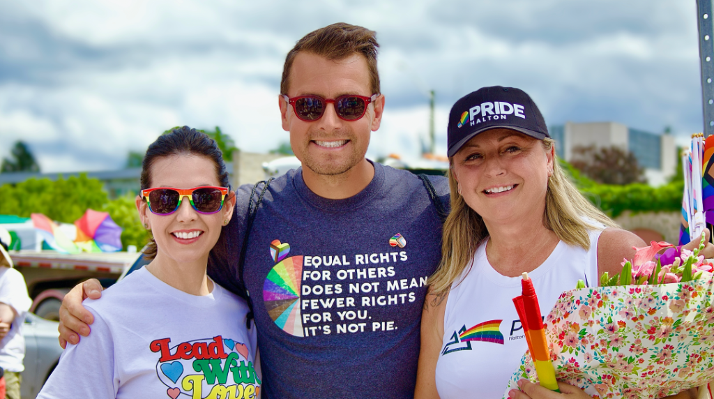 Pride Halton founder Melanie Tremills (centre, holding flowers) with Members of Parliament Kristina Tesser Derksen (left) and Adam van Koeverden (right) at a Pride Halton celebration.