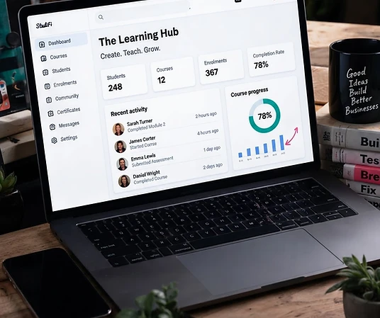 A laptop showing The Learning Hub, surrounded by a phone, coffee and notes on Katie’s desk