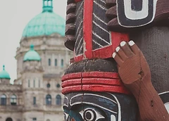 A carved totem pole with the Parliament Buildings in the background