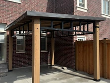 An angled view of a wooden pergola structure installed against a brick house wall.