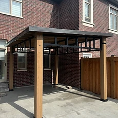 An angled view of a wooden pergola structure installed against a brick house wall.