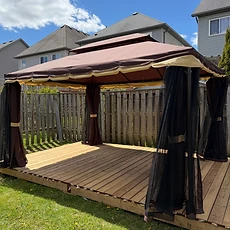 A completed gazebo with brown fabric canopy and curtains on a wooden deck in a backyard.