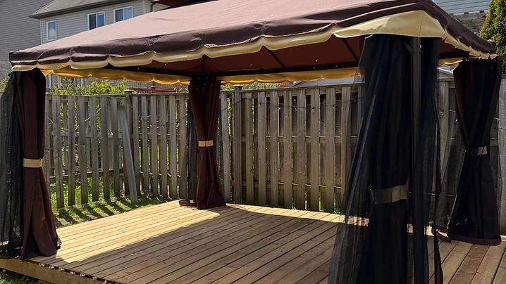 A completed gazebo with brown fabric canopy and curtains on a wooden deck in a backyard.
