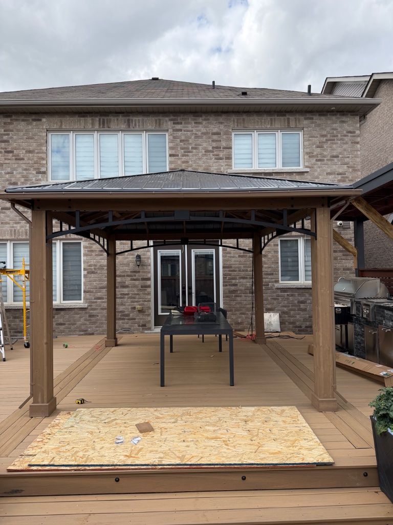 A black metal gazebo installed on a concrete patio next to a brick house.