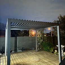 A modern louvered pergola installed on a wooden deck at night.