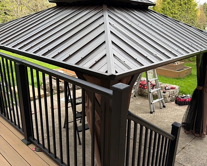 A gazebo frame stands on a patio next to a stack of shipping cardboard boxes.