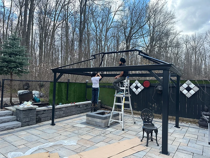 Two technicians working on the frame of a black metal gazebo.