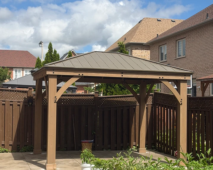 A wooden pergola stands on a concrete patio in a backyard with potted plants nearby.