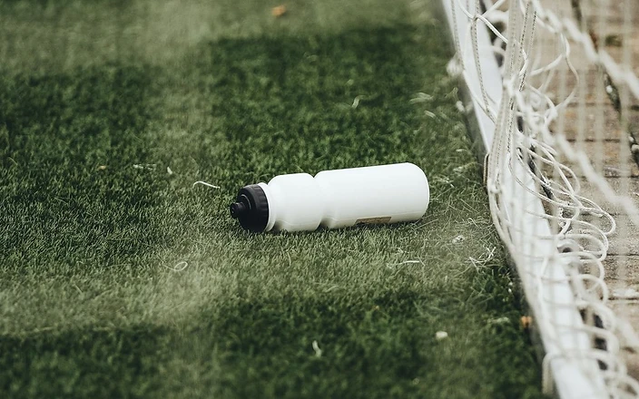 A water bottle on an artificial grass pitch beside a goal net