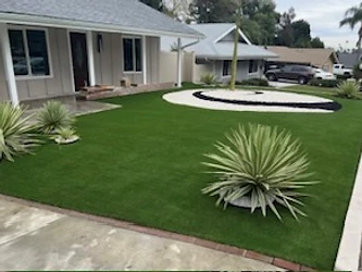 Front yard artificial turf with circular decorative rock feature and brick edging