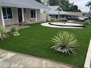 Front yard artificial turf with concrete curb border and circular stone feature