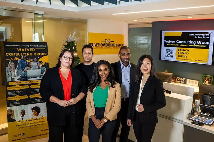 The Waiver Consulting Group team standing together beside the firm branded reception wall