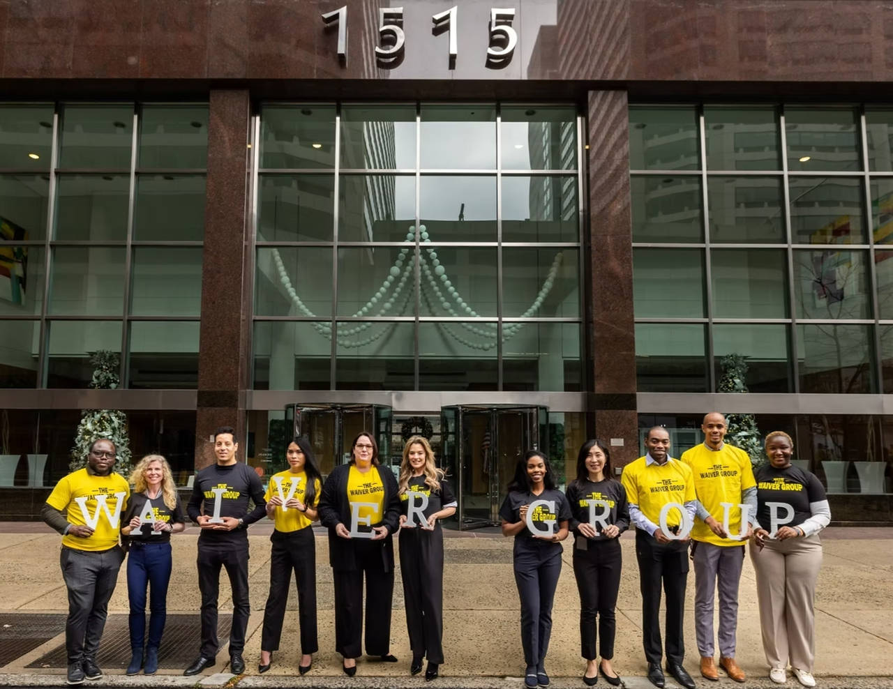 The Waiver Group team standing outside the firm's headquarters holding letters that spell WAIVER GROUP