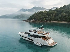 A sleek luxury motor yacht anchored in calm turquoise water off a lush Koh Samui coastline