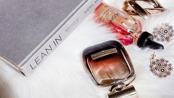 Beauty objects including a book, perfume bottle, and beauty oil on a white fur surface