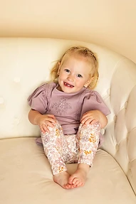 A smiling toddler with blonde hair sitting on a cream tufted chair.