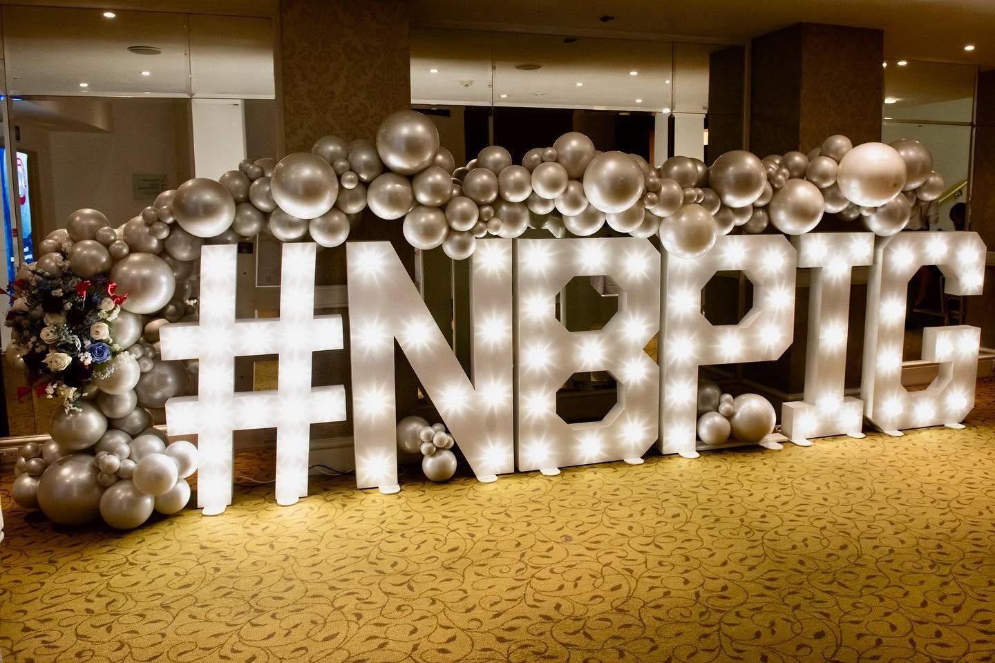 #NBPIG light-up letters framed by a silver balloon arch