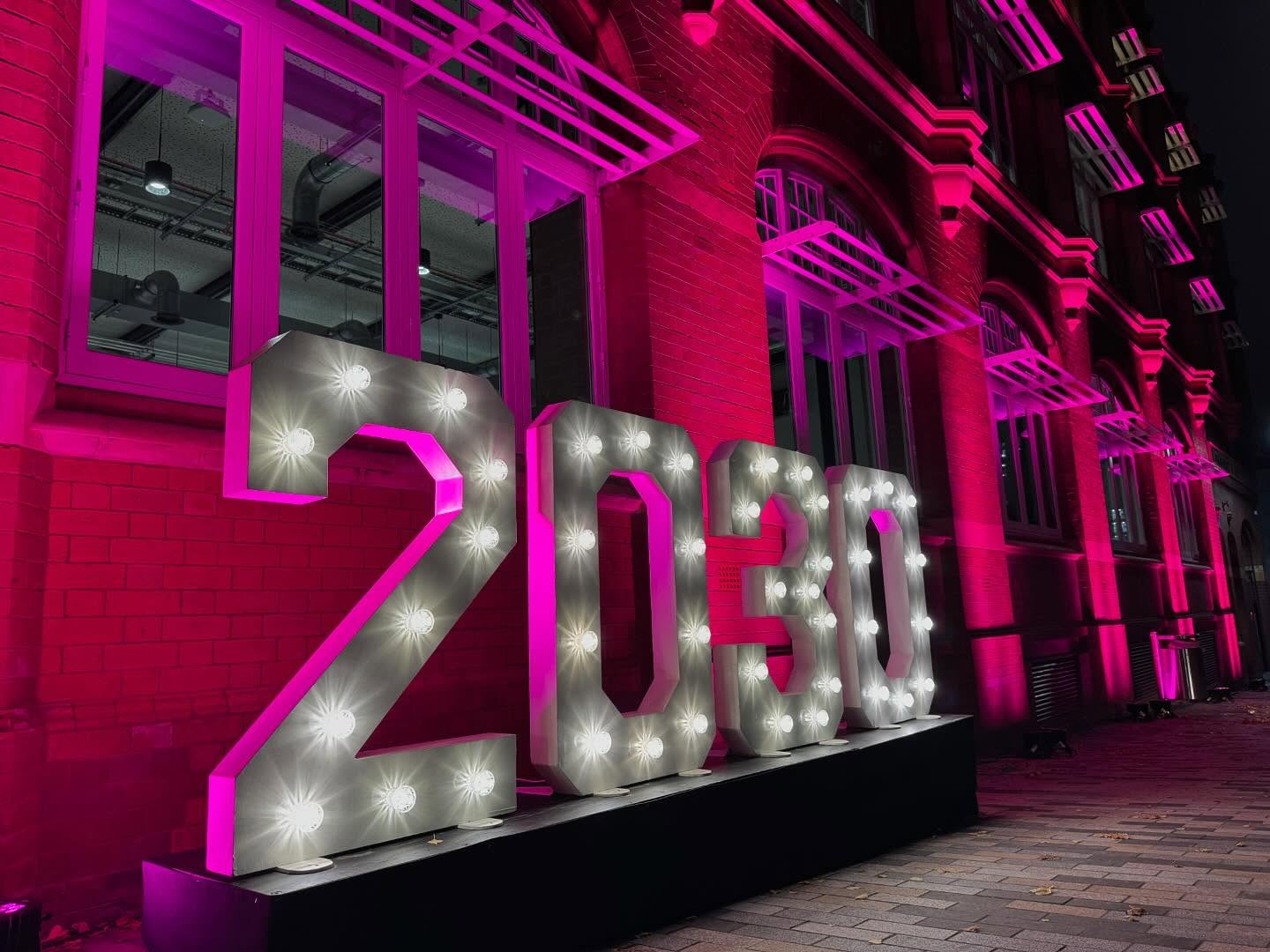 Light-up numbers 2030 against a magenta-lit brick building