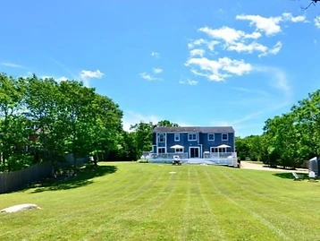 Two-story house viewed across a striped mowed lawn under a bright blue sky