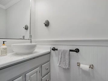 Bathroom vanity with white vessel sink, coconut-vanilla soap, and beadboard wainscoting