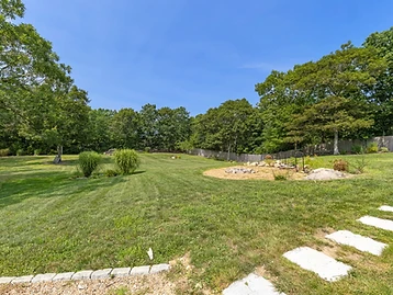 Wide open backyard with mowed lawn, fire pit area, and trees beyond