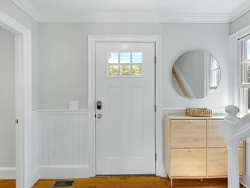 The front entry with a white craftsman door, round mirror, and rattan sideboard