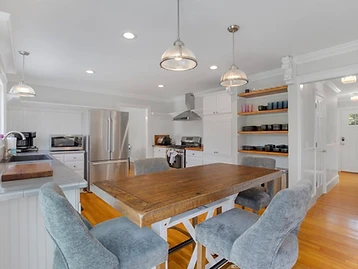 The kitchen with a rustic wood island, white cabinetry, and open shelving