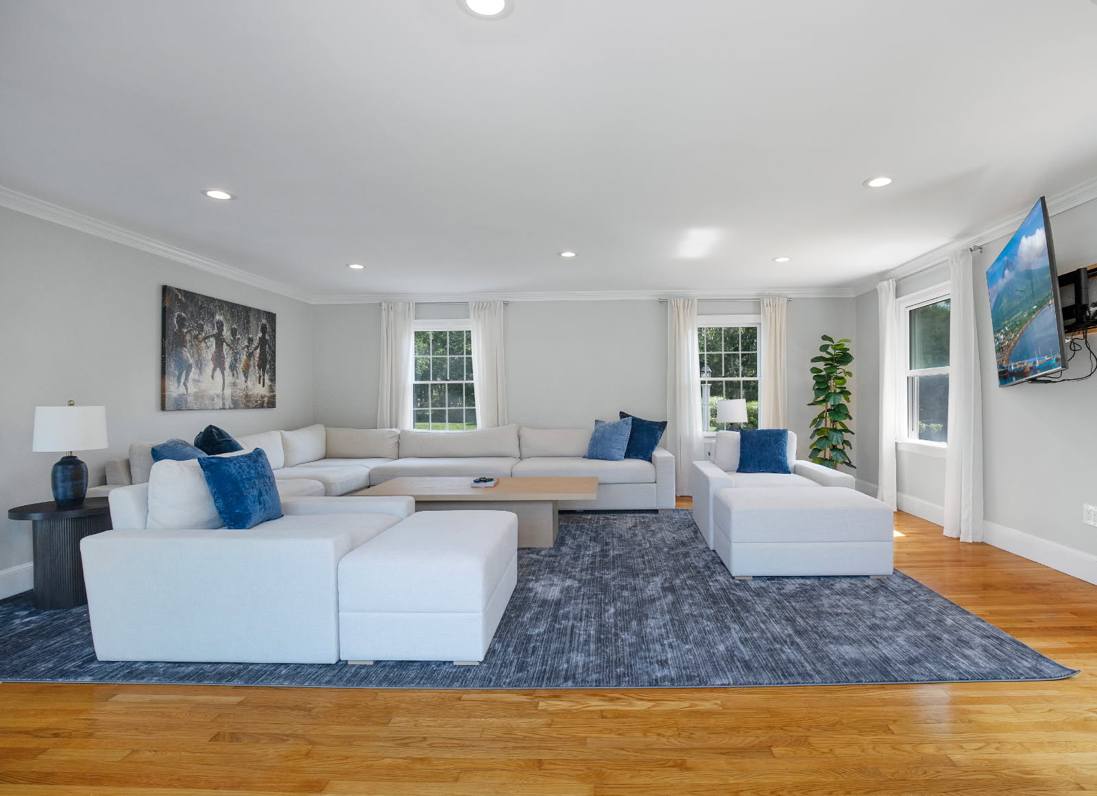The living room with a cream U-shaped sectional, deep-blue rug, and tall curtained windows