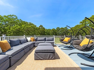 The back deck with grey sectional, two hanging egg chairs, and woven rug