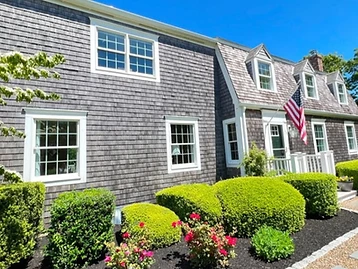 Angular exterior view of the shingled house with gabled dormers, white portico, and American flag