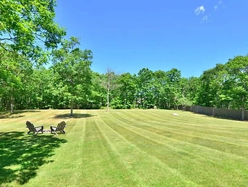 Expansive backyard lawn with two Adirondack chairs and a wooden fence bordered by mature trees