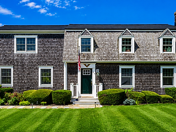 Front facade of the cedar-shingled two-story house with a green door, dormer windows, and manicured lawn