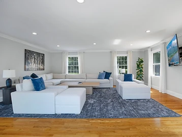 The living room with a light-grey sectional, blue rug, light-wood coffee table, and wall-mounted coastal TV