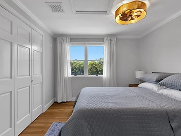 Bedroom with grey coverlet, white closet doors, and garden-view window