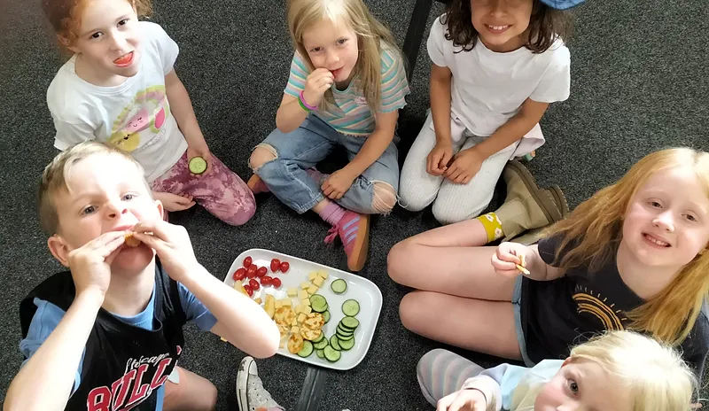 Children sitting in a circle on the carpet sharing a snack together