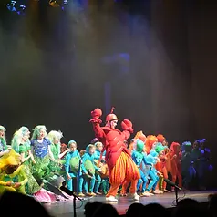 Wide ensemble scene of students in sea-creature costumes under stage lighting