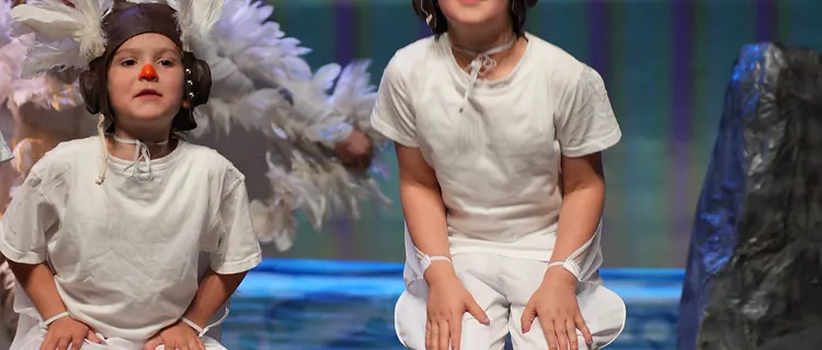 Two students dressed as birds performing on stage with a painted sea backdrop