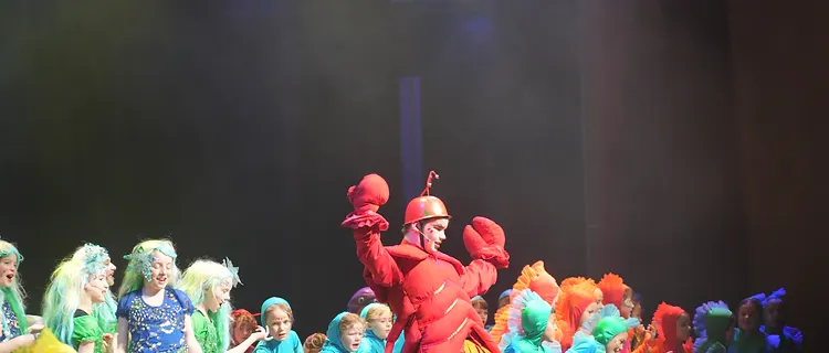 Wide ensemble scene of students in sea-creature costumes under stage lighting
