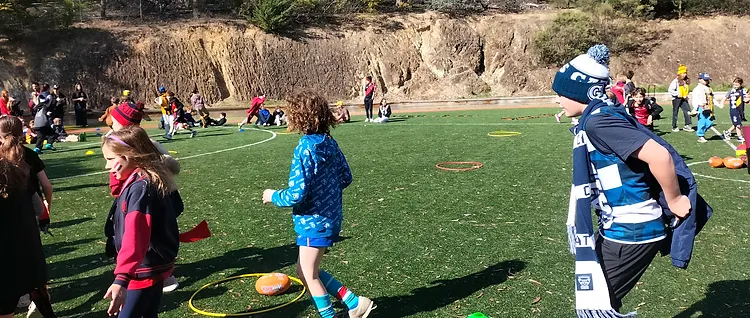 Students in team scarves and beanies taking part in an AFL-themed sports activity on the turf