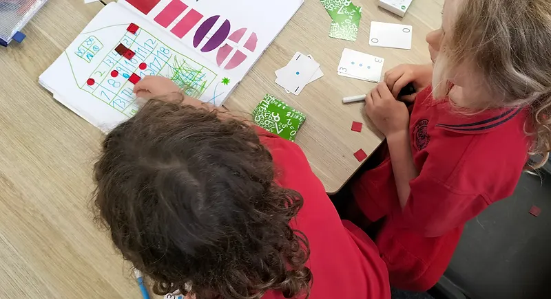 Two students working on a maths grid activity with cards and counters